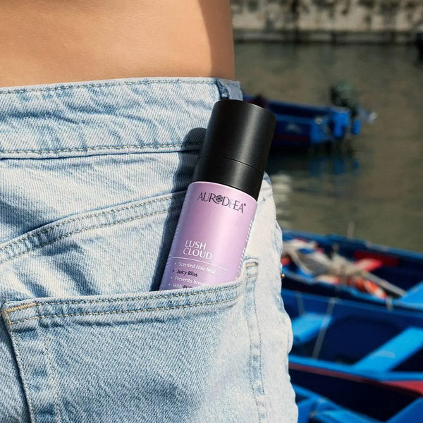 Aurodhea Lush Cloud SHM001 Juicy Bliss – Frau hält Haarparfüm-Spray in der Jeanstasche, am Wasser, lässiger Lifestyle-Look