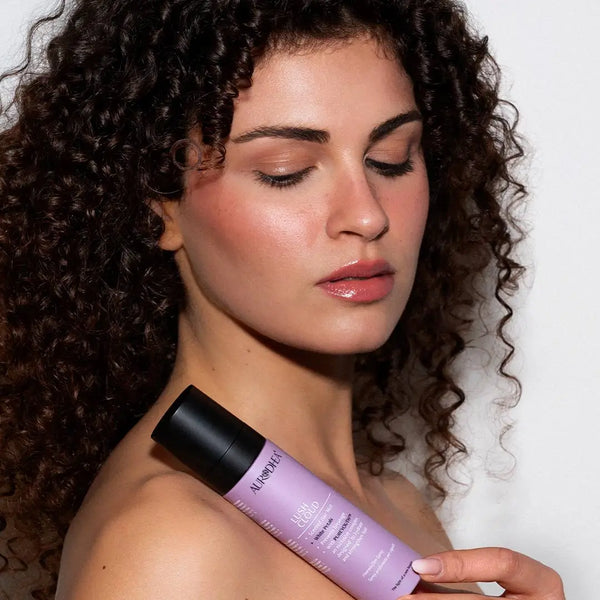 Aurodhea Lush Cloud SHM003 White Petals – Frau mit lockigem Haar hält Haarparfüm-Spray, eleganter Lifestyle-Look