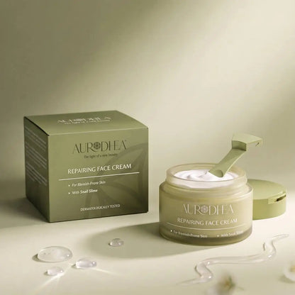 Aurodhea Repairing Face Cream mit Schneckenschleim in geöffnetem Tiegel mit Spatel und Verpackung