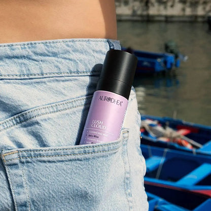 Aurodhea Lush Cloud SHM001 Juicy Bliss – Frau hält Haarparfüm-Spray in der Jeanstasche, am Wasser, lässiger Lifestyle-Look