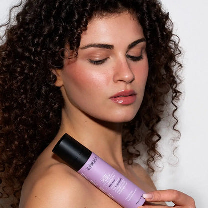 Aurodhea Lush Cloud SHM003 White Petals – Frau mit lockigem Haar hält Haarparfüm-Spray, eleganter Lifestyle-Look