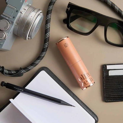 Orangefarbenes Olfazeta Parfüm-Taschenetui Modern auf Schreibtisch mit Kamera, Brille und Notizbuch