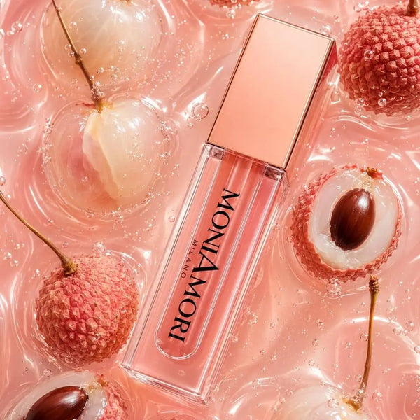 MoniAmori Juicy Oil Lychee MM062 – Lippenöl-Flakon liegt zwischen frischen Litschis in pinkfarbenem Wasser, Lifestyle-Aufnahme