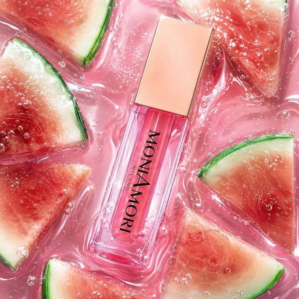 MoniAmori Juicy Oil Watermelon MM064 – pinkfarbener Lippenöl-Flakon liegt zwischen frischen Wassermelonenstücken in pinkfarbenem Wasser, Lifestyle-Aufnahme