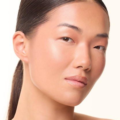 Model mit MoniAmori Light & Go Highlighter Stick: Frau mit strahlendem Teint und leuchtenden Akzenten auf den Wangenknochen, natürliches Make-up mit Glow-Effekt, leicht seitliche Porträtaufnahme.
